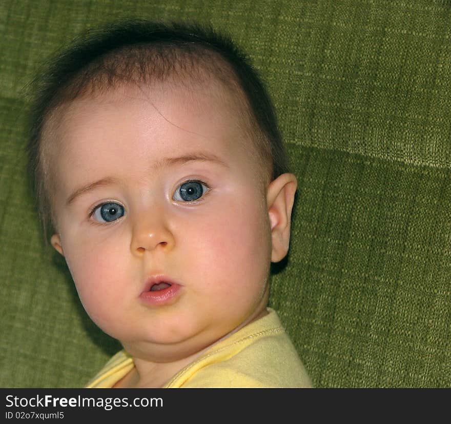 Puzzled-looking toddler sitting on a green sofa