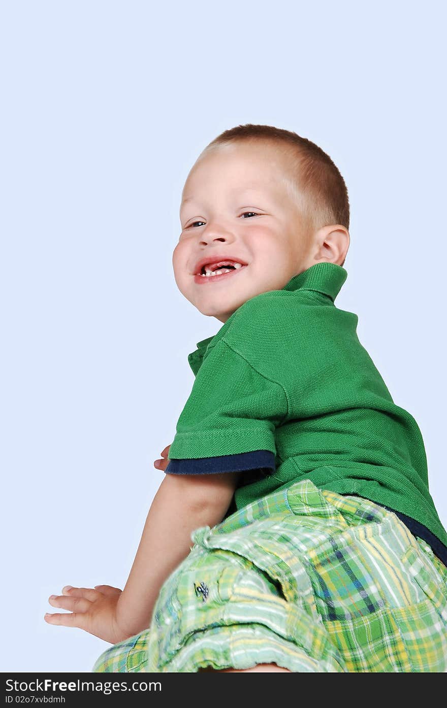 An young toddler boy has fun playing on the floor in the studio, shooing his missing tooth, in a green outfit on light blue background. An young toddler boy has fun playing on the floor in the studio, shooing his missing tooth, in a green outfit on light blue background.