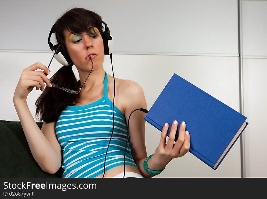 Pretty girl sitting on a sofa and listening to a book. Pretty girl sitting on a sofa and listening to a book.