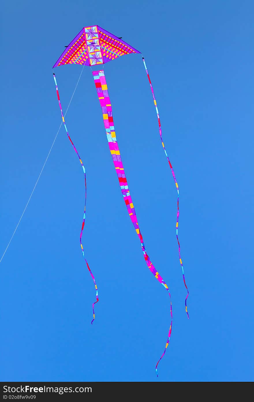 Colorful kite flying high in bright blue sky.