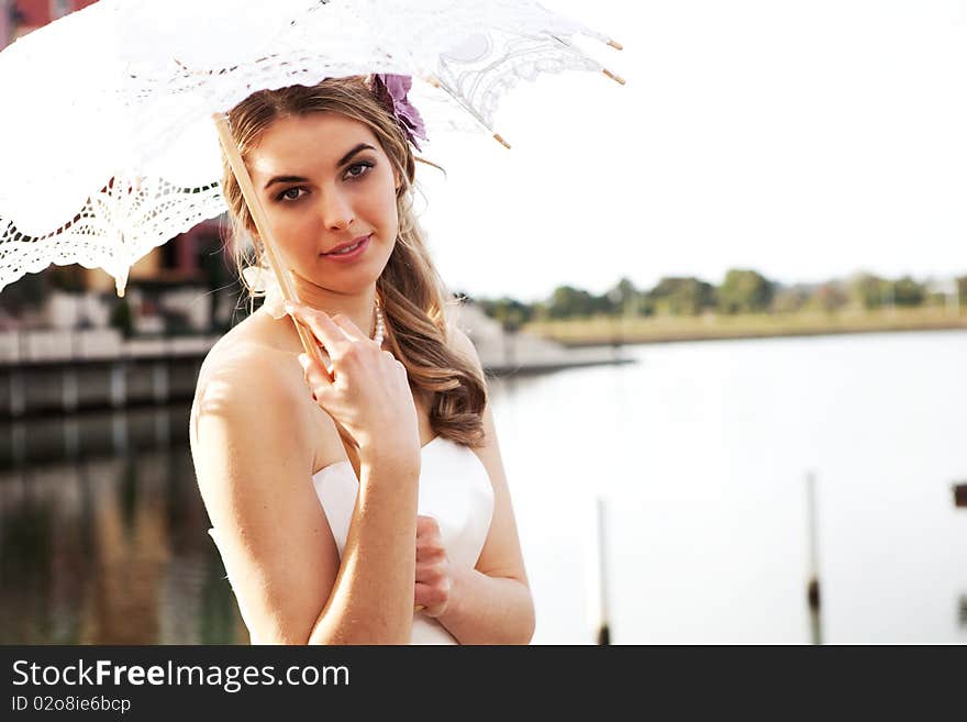 An attractive young woman in a gown is smiling and holding a parasol near the water. Horizontal shot. An attractive young woman in a gown is smiling and holding a parasol near the water. Horizontal shot.