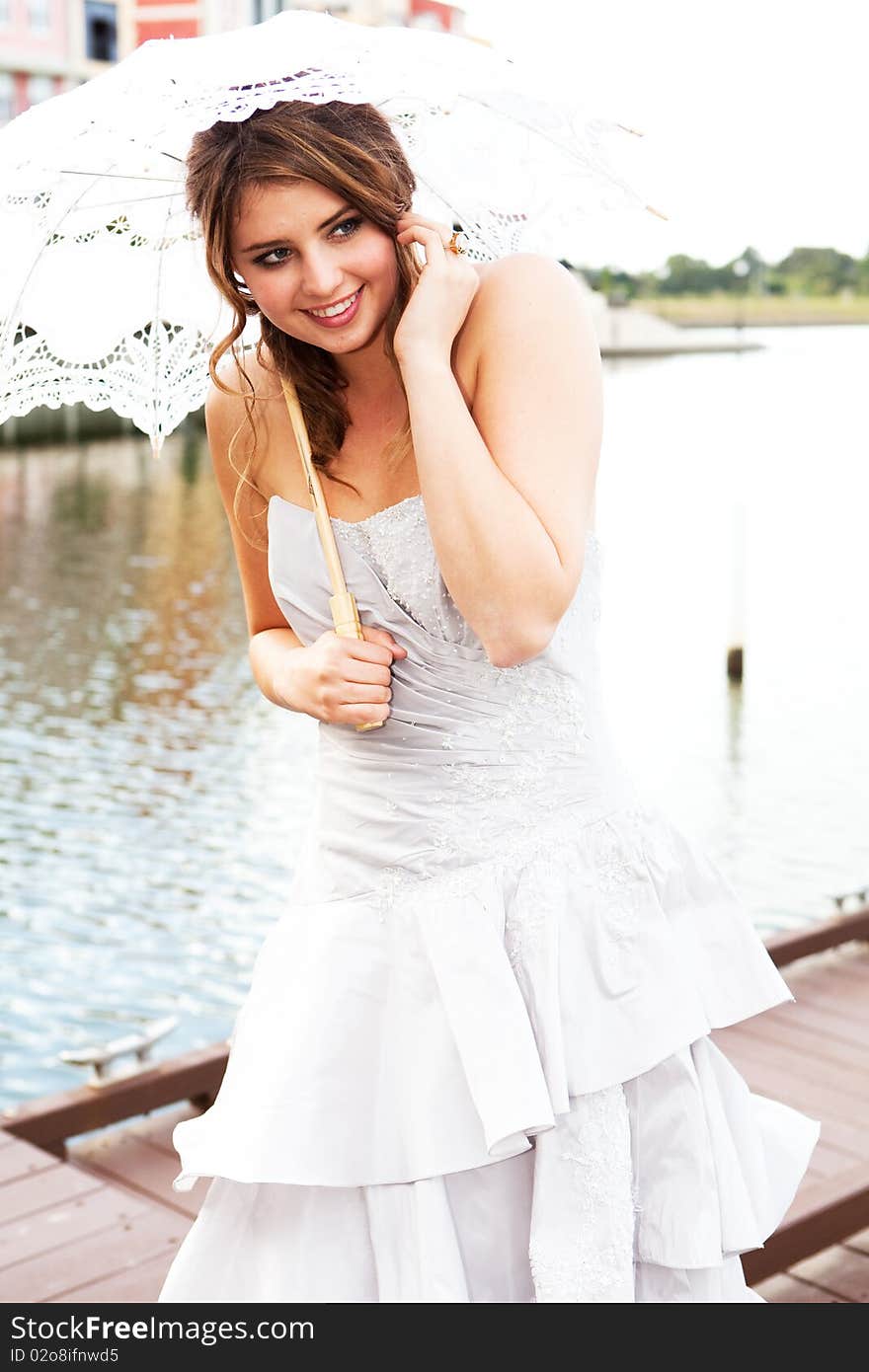 An attractive young woman in a gown is smiling and holding a parasol near the water. Vertical shot. An attractive young woman in a gown is smiling and holding a parasol near the water. Vertical shot.