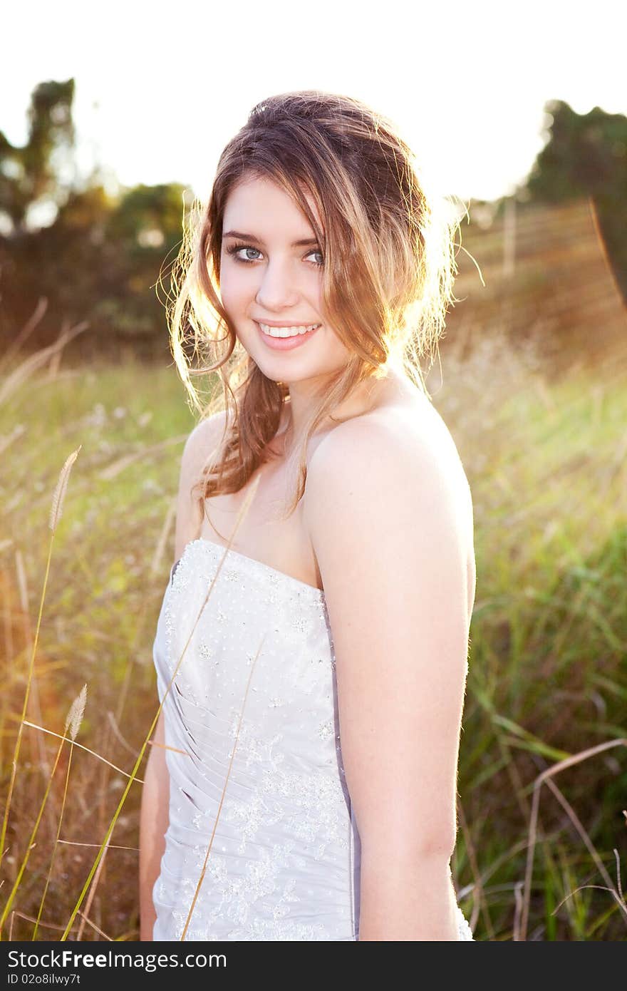 An attractive young woman wearing formal attire is standing in a grass field. Vertical shot. An attractive young woman wearing formal attire is standing in a grass field. Vertical shot.