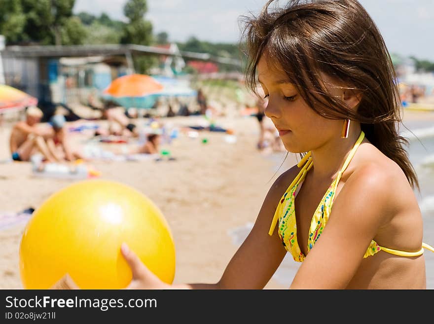 Little girl plays ball at crowded seaside