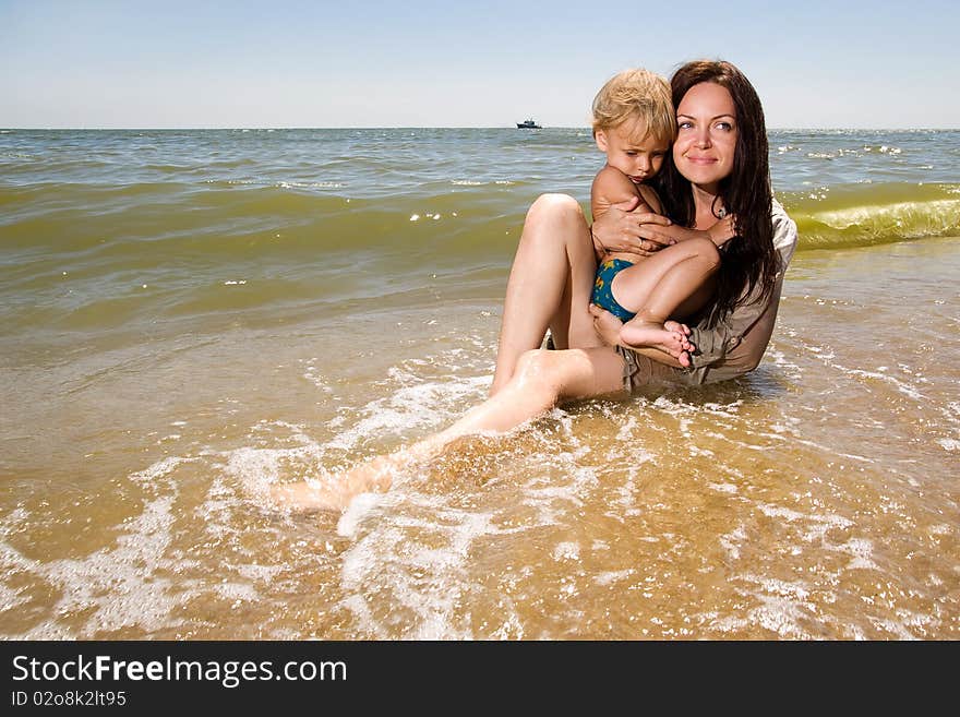 Young mom holds her little son in hands sitting in water of a sea. Young mom holds her little son in hands sitting in water of a sea