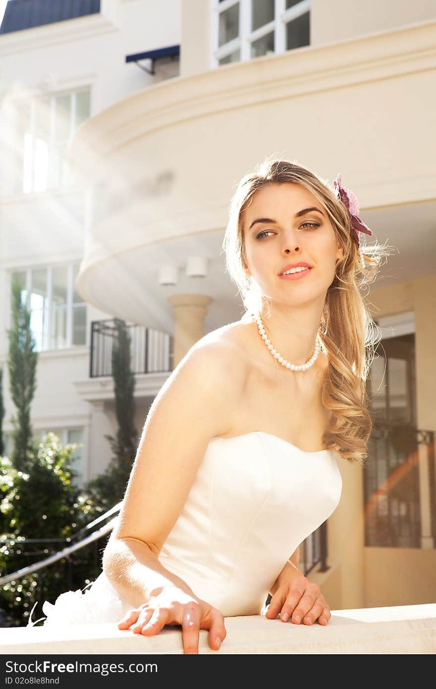 An attractive young woman is wearing a white dress and pearls and is smiling. She is looking over a railing. Vertical shot. An attractive young woman is wearing a white dress and pearls and is smiling. She is looking over a railing. Vertical shot.