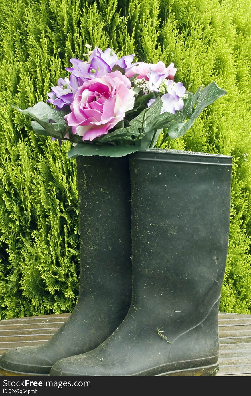 Flowers in a wellington on a garden table against a shrub. Flowers in a wellington on a garden table against a shrub