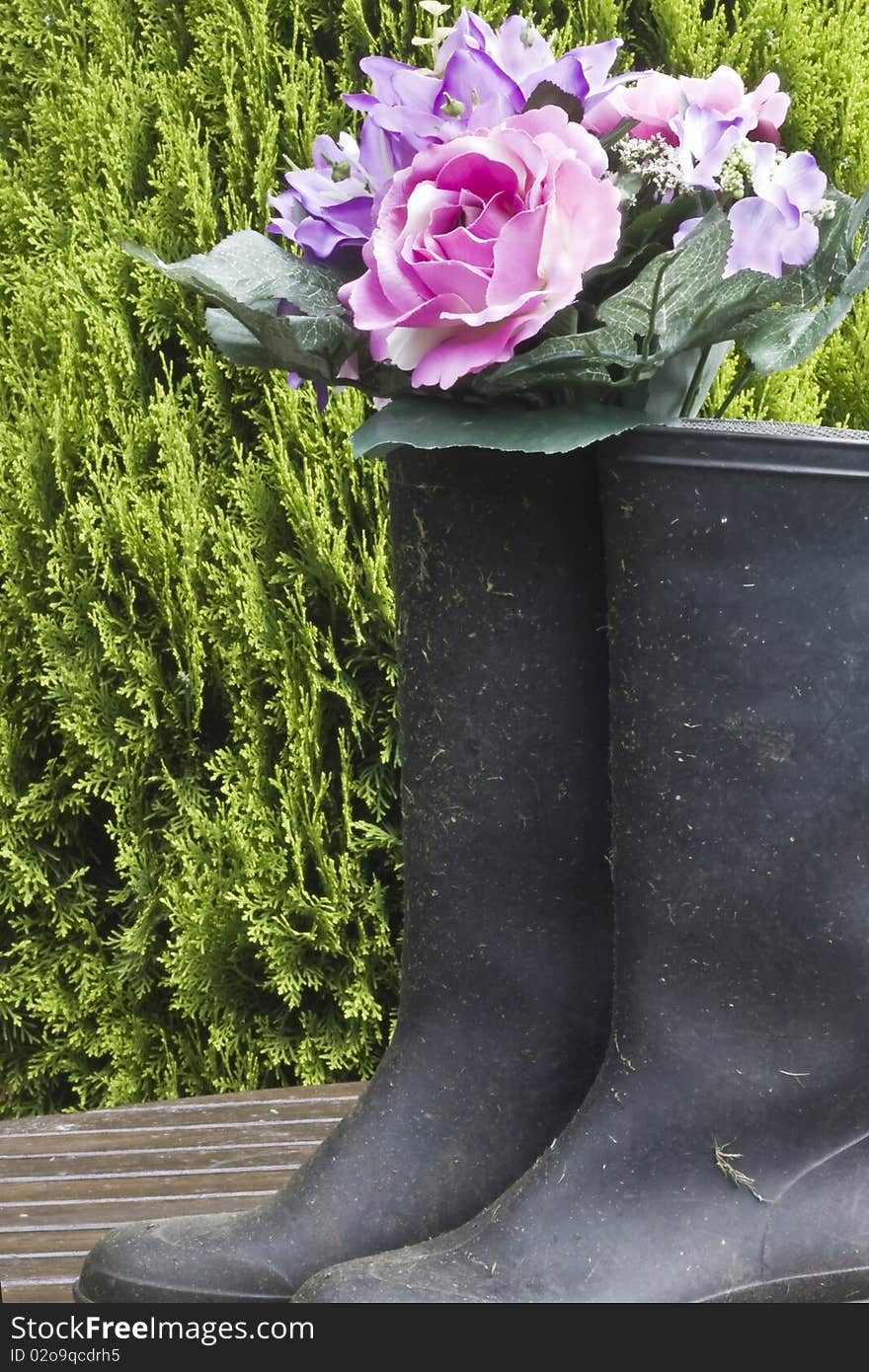 Flowers in a wellington on a garden table against a shrub. Flowers in a wellington on a garden table against a shrub