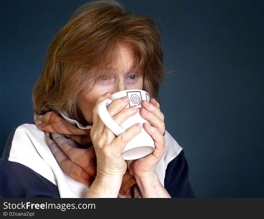 Head and shoulders of adult redhead Female with scarf rugged around neck and hands wrapped around a comforting mug of hot drink, wistfully looking into the distance. Isolated with bluish background. Head and shoulders of adult redhead Female with scarf rugged around neck and hands wrapped around a comforting mug of hot drink, wistfully looking into the distance. Isolated with bluish background.