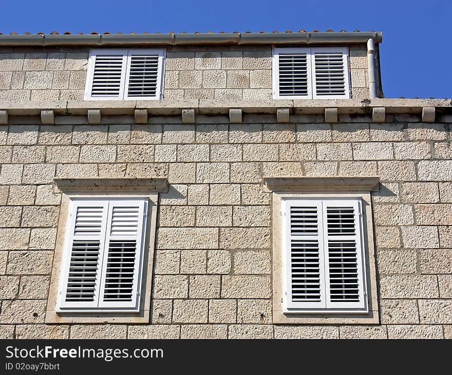 Details of the stony building facade with white shutters.