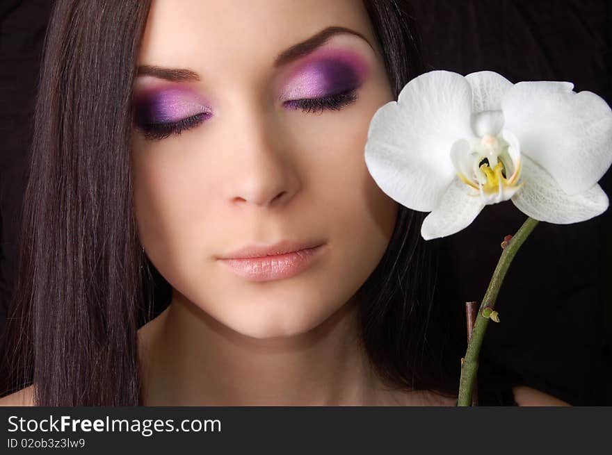 Beautiful brunette with orchid flower eyes closed isolated on black