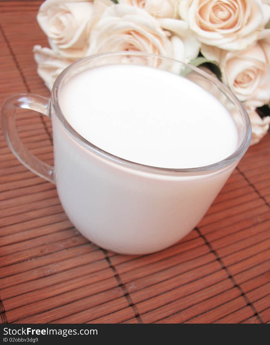 Cup of fresh,white milk and creamy roses isolated on wooden background. Cup of fresh,white milk and creamy roses isolated on wooden background