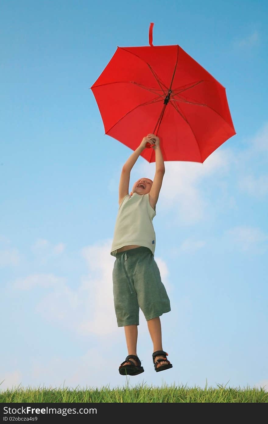 White boy flying on a red umbrella and laughing against the blue summer sky. White boy flying on a red umbrella and laughing against the blue summer sky