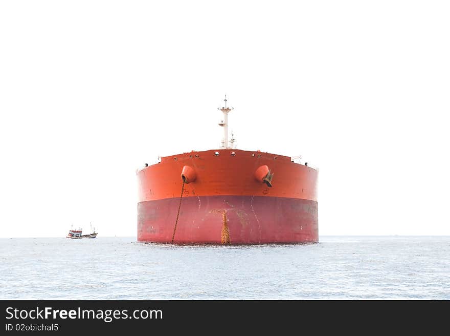 High key photo of orange oil tanker at anchor with the sky completely white. Small fishing vessel to the left. High key photo of orange oil tanker at anchor with the sky completely white. Small fishing vessel to the left.