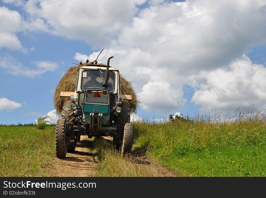 A tractor with the trailer the loaded hay on summer soil field road. A tractor with the trailer the loaded hay on summer soil field road.