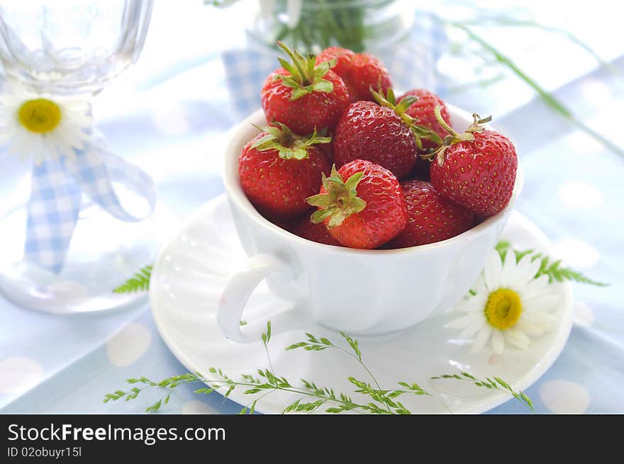 A cup of strawberries with daisy on light blue background. A cup of strawberries with daisy on light blue background