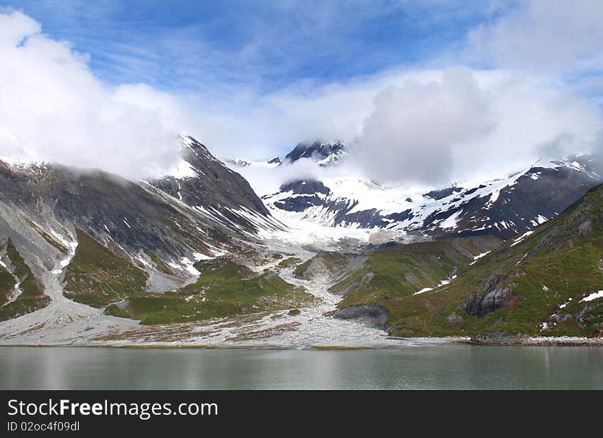 Scenic view of snowy mountains and sunshine in Alaska. Blue sky peeking through clouds. Scenic view of snowy mountains and sunshine in Alaska. Blue sky peeking through clouds.