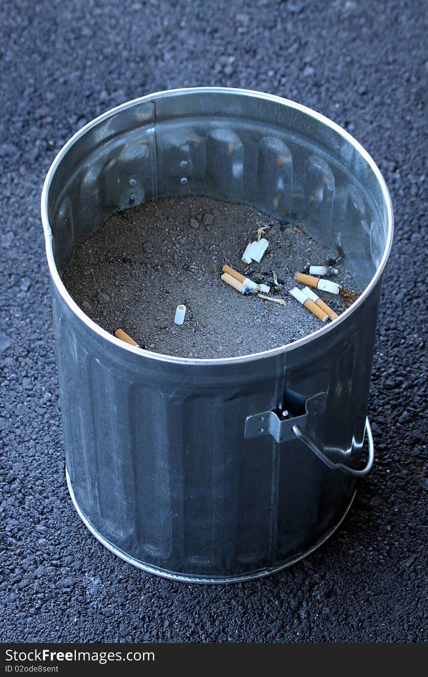 A small bucket used as a cigarette ashtray, filled with sand and used cigarette butts visible inside. A small bucket used as a cigarette ashtray, filled with sand and used cigarette butts visible inside.