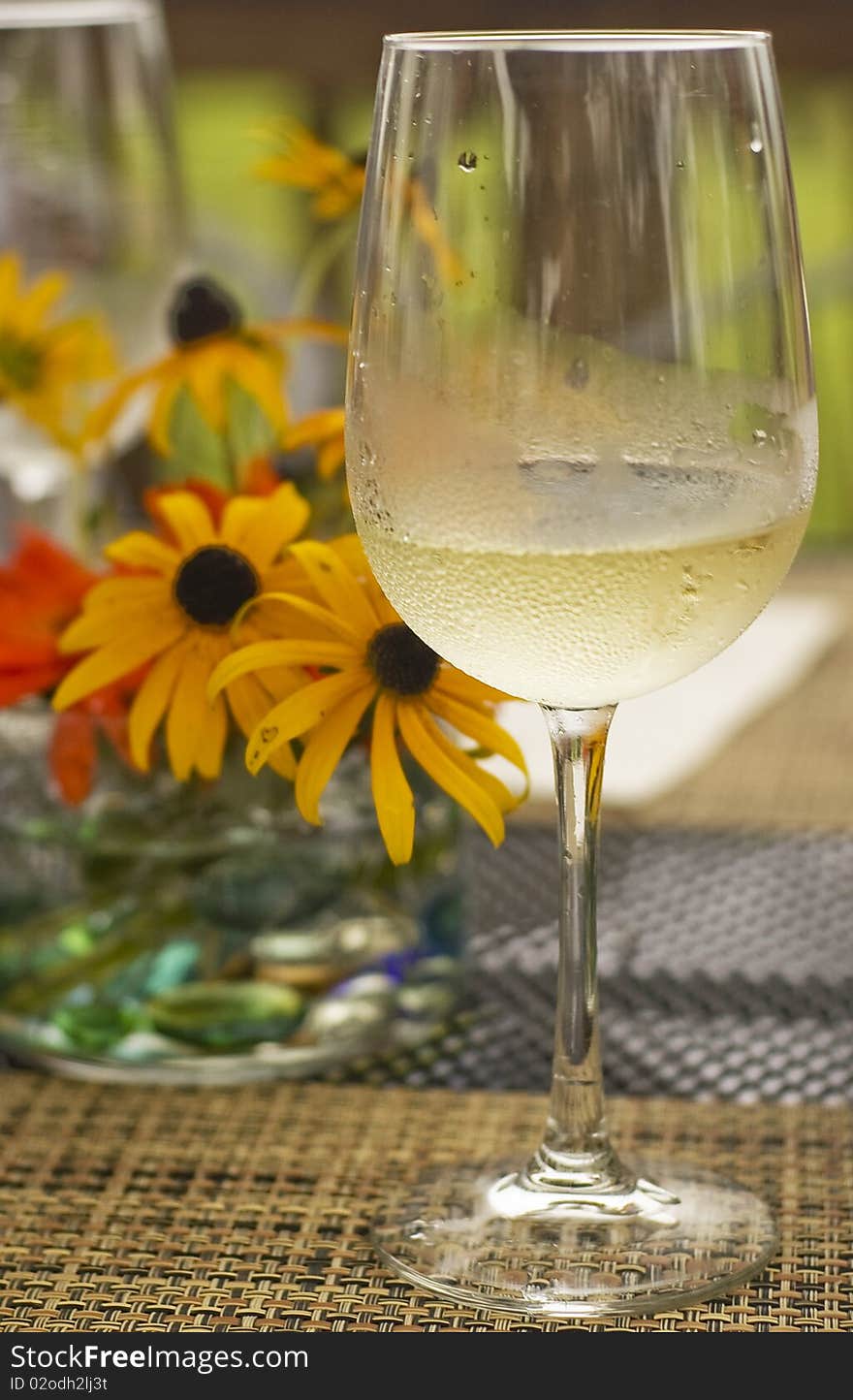 Glass of chilled white wine standing on a rustic mat with yellow flowers on the background