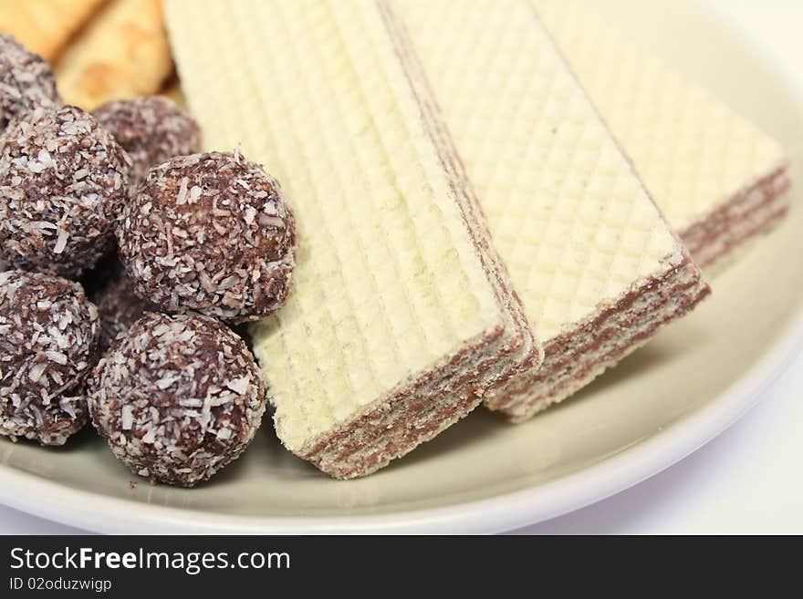 Various confectionery on plate, chocolate balls, wafer witch chocolate layers and cookies on white background