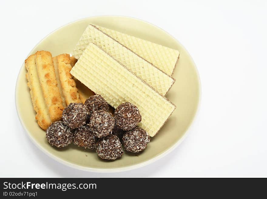 Various confectionery on plate, chocolate balls, wafer witch chocolate layers and cookies on white background