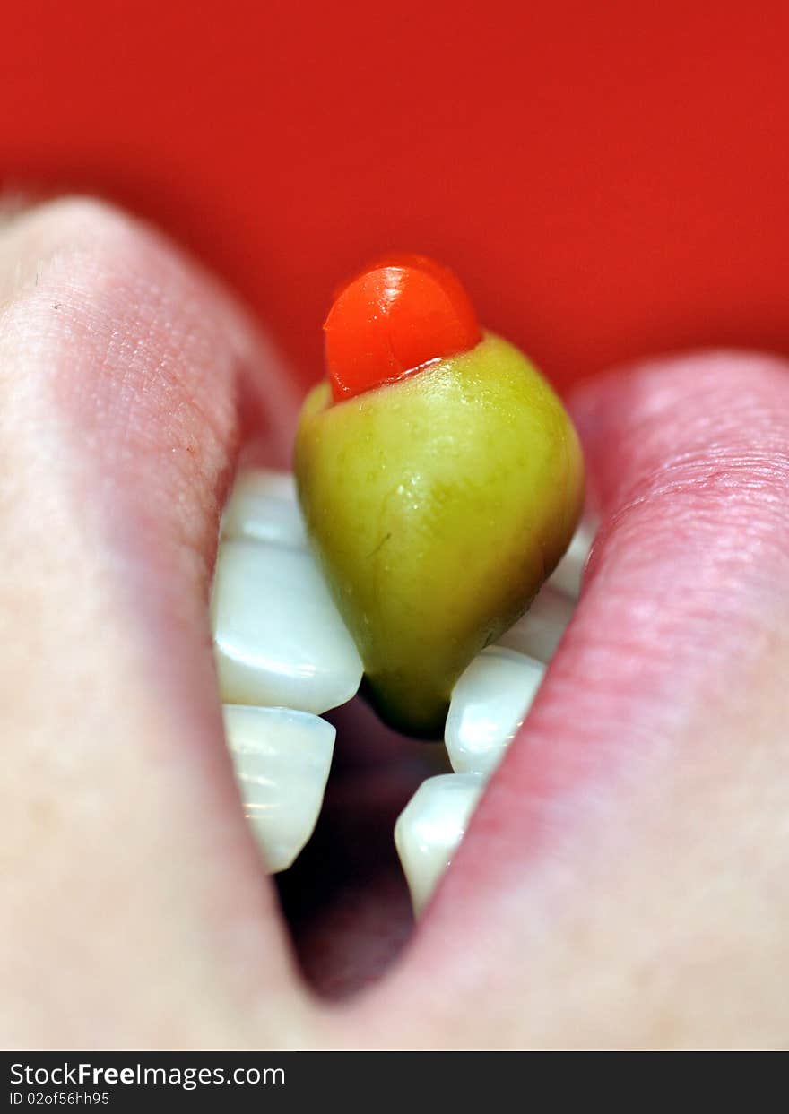 A green olive held in girls teeth beneath wet lips. A green olive held in girls teeth beneath wet lips