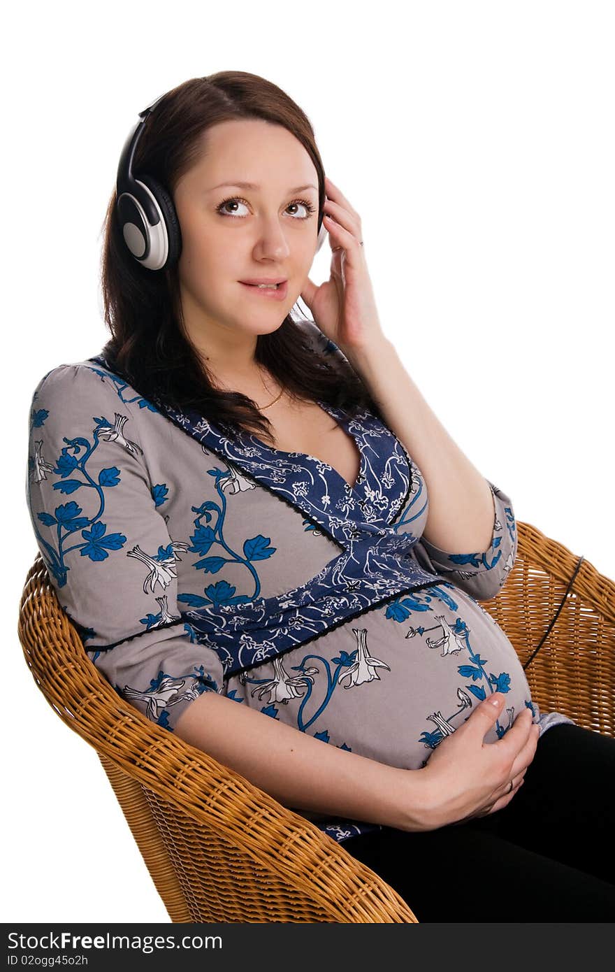 Beautiful pregnant woman sits in a wicker chair and listens to music, isolated on white. Beautiful pregnant woman sits in a wicker chair and listens to music, isolated on white