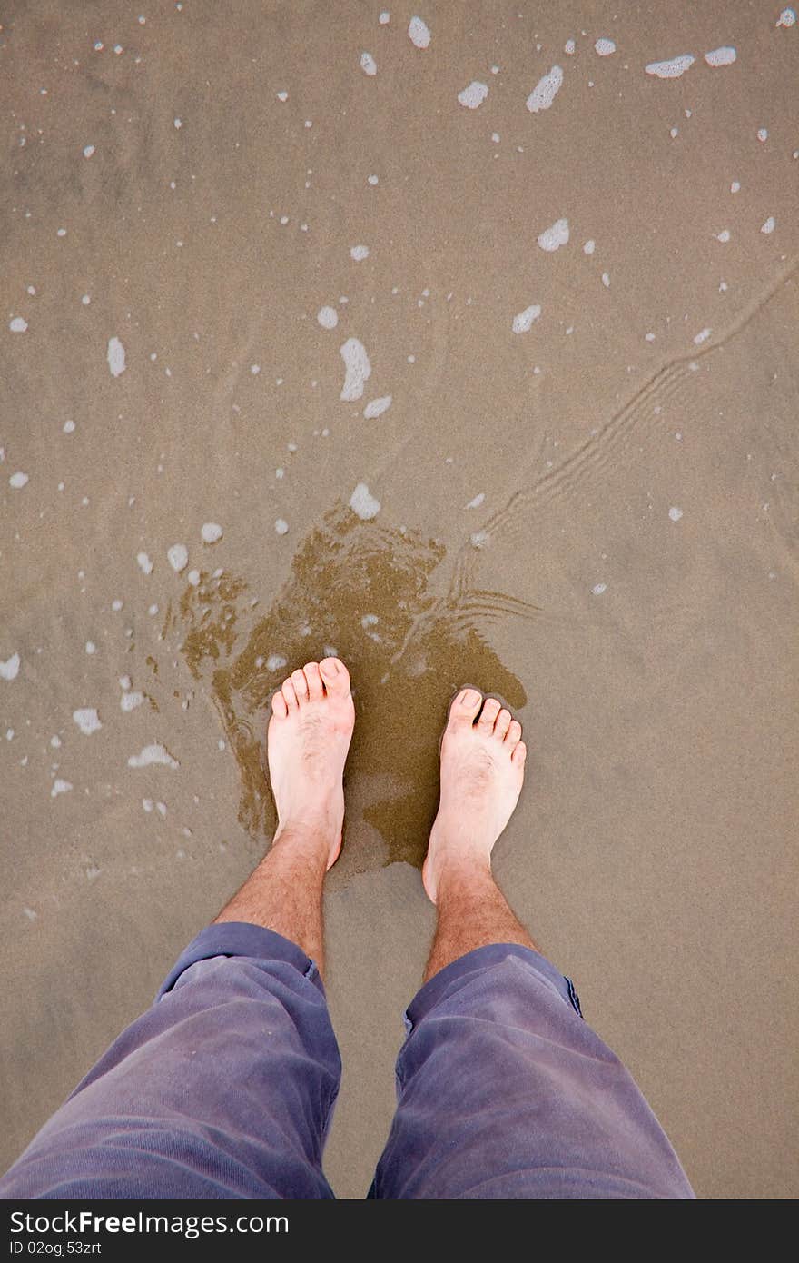 A man's feet in the water at the beach along the Oregon Coast whie barefoot and wading in the ocean. A man's feet in the water at the beach along the Oregon Coast whie barefoot and wading in the ocean.