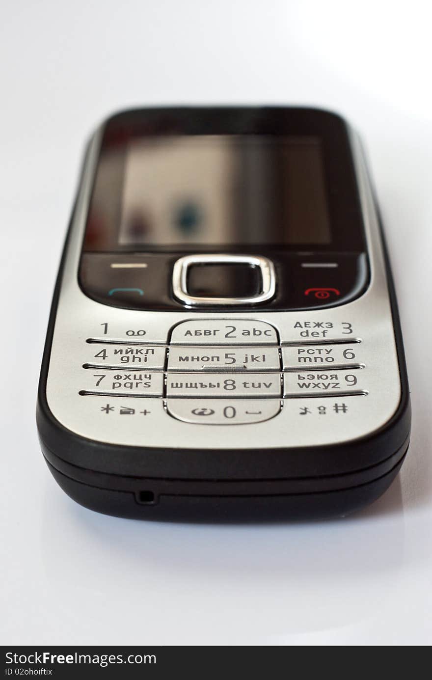 Mobile telephone with black and silver body lies on a white surface