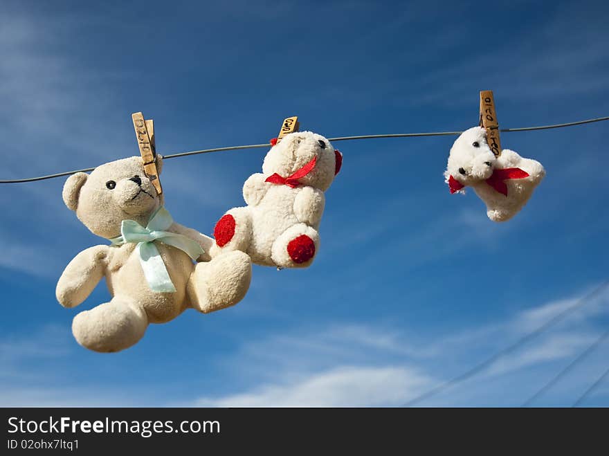 Three teddies hung out to dry on a clothesline, with blue skies in the background