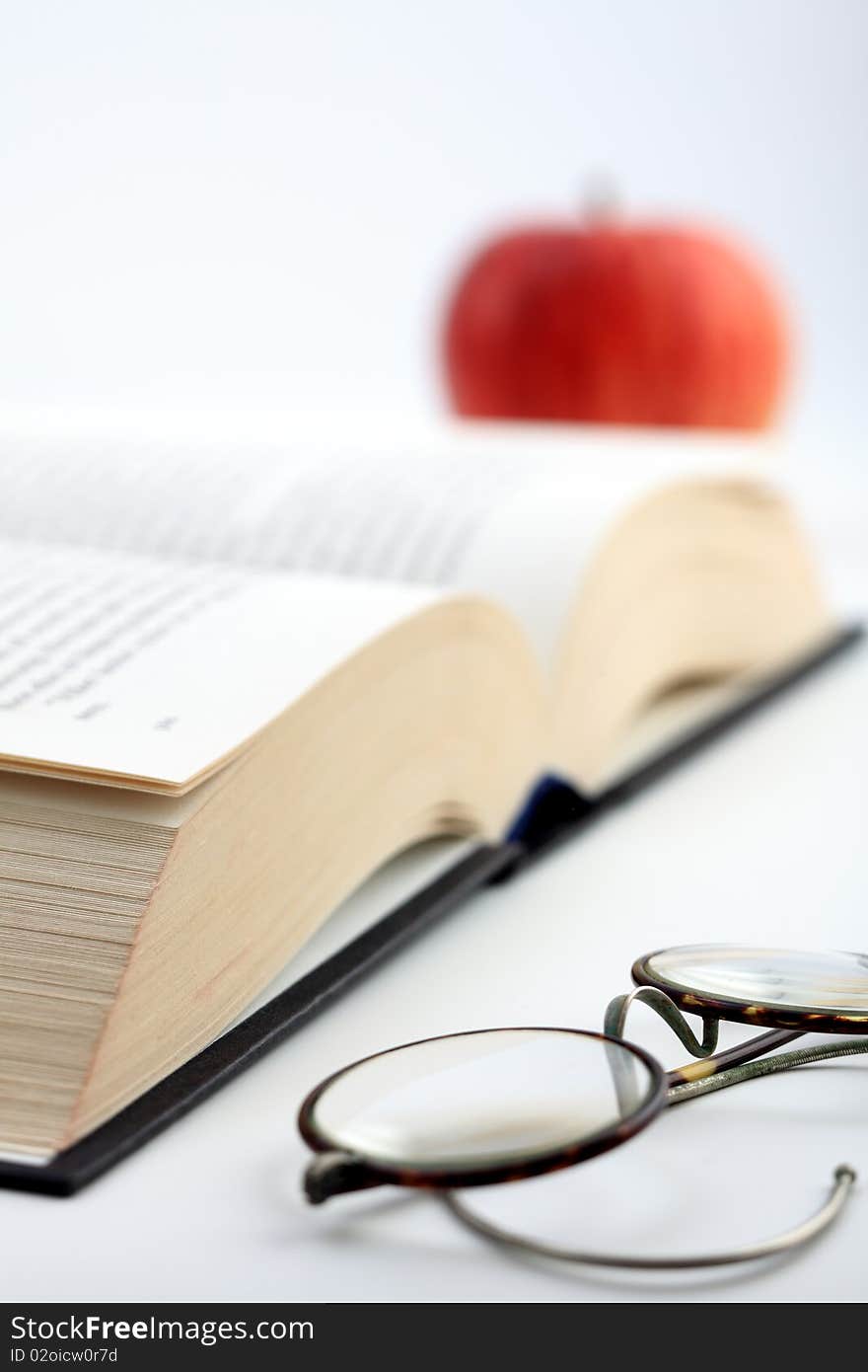 An open book, glasses and an apple. An open book, glasses and an apple