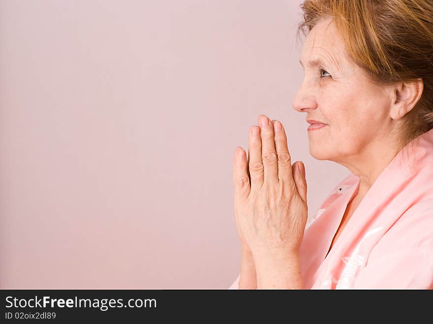 Elderly woman praying on a pink background