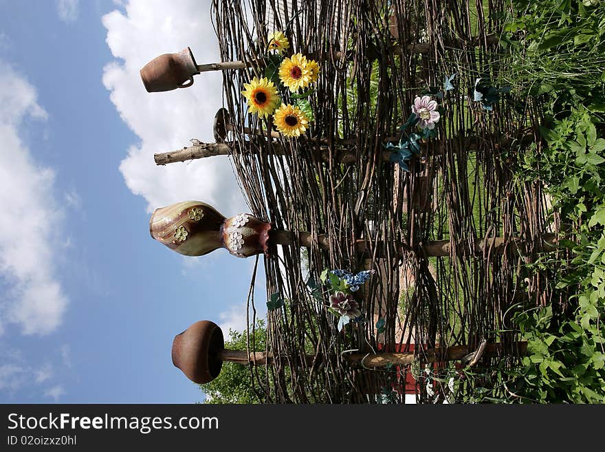 Rural fence with jugs and sunflowers against the sky