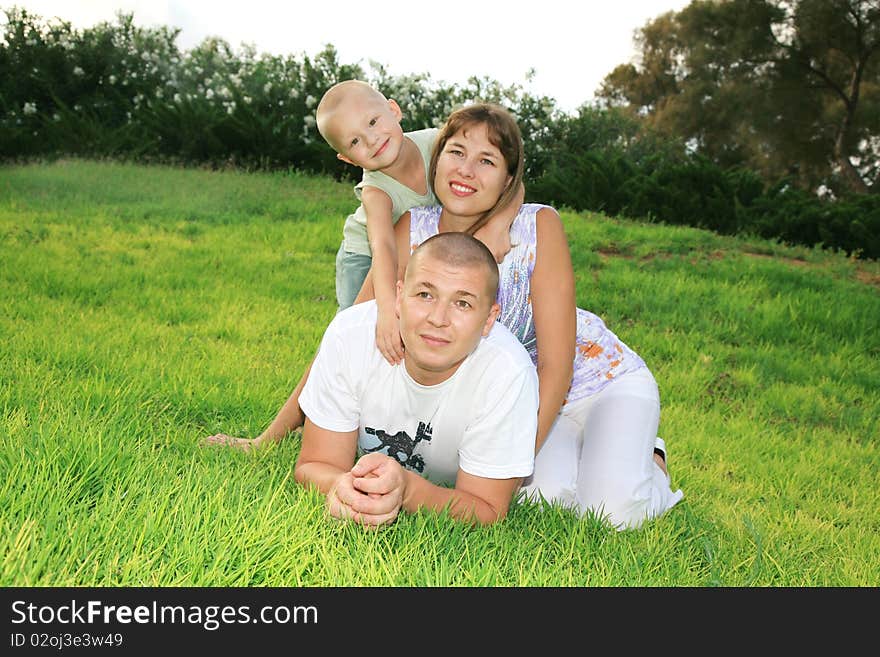 Beautiful young family fun playing together in a city park on the green grass. Beautiful young family fun playing together in a city park on the green grass