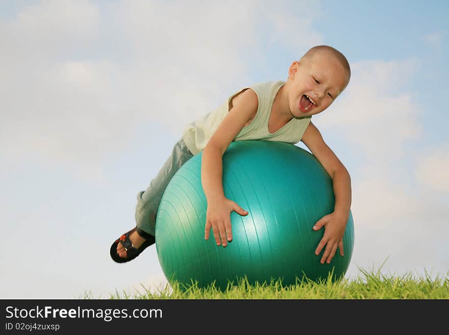 Little white boy fun playing on a gymnastic ball, laughing and enjoying the green grass and the blue sky. Little white boy fun playing on a gymnastic ball, laughing and enjoying the green grass and the blue sky.