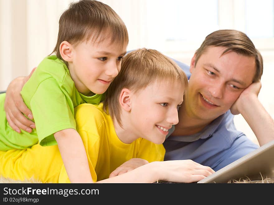 Father with  sons is on the carpet with laptop. Father with  sons is on the carpet with laptop