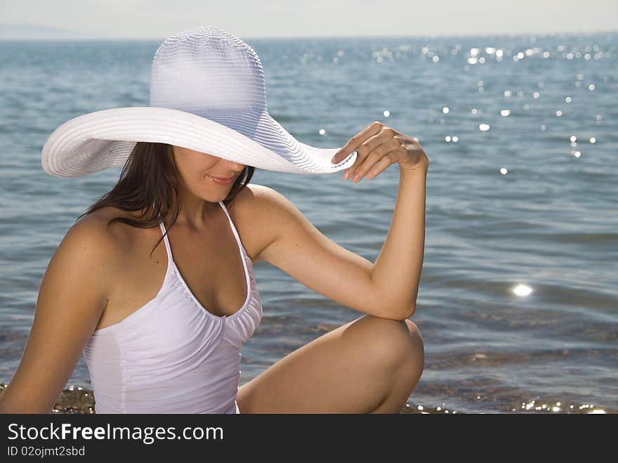 Tanned young girl in a white beach hat against the blue sea. Tanned young girl in a white beach hat against the blue sea