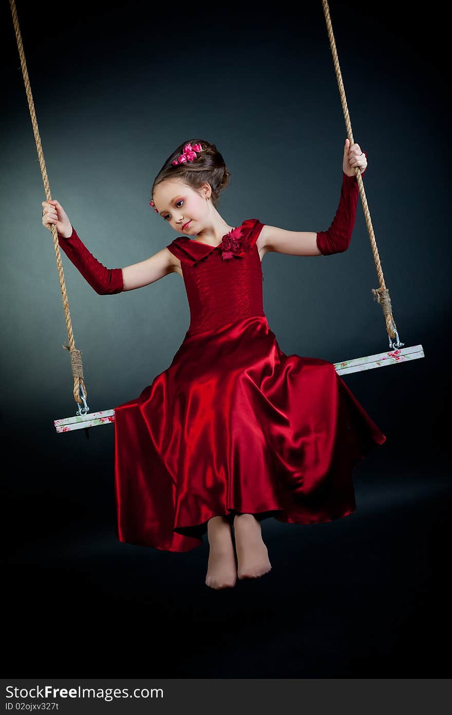 Young model in red dress on swing on black background. Young model in red dress on swing on black background