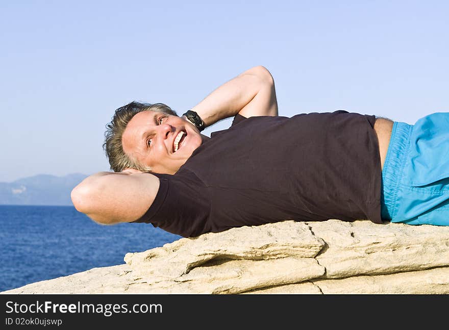 A color portrait photo of a smiling man in his forties laying on a rock and relaxing during his vacation. A color portrait photo of a smiling man in his forties laying on a rock and relaxing during his vacation.