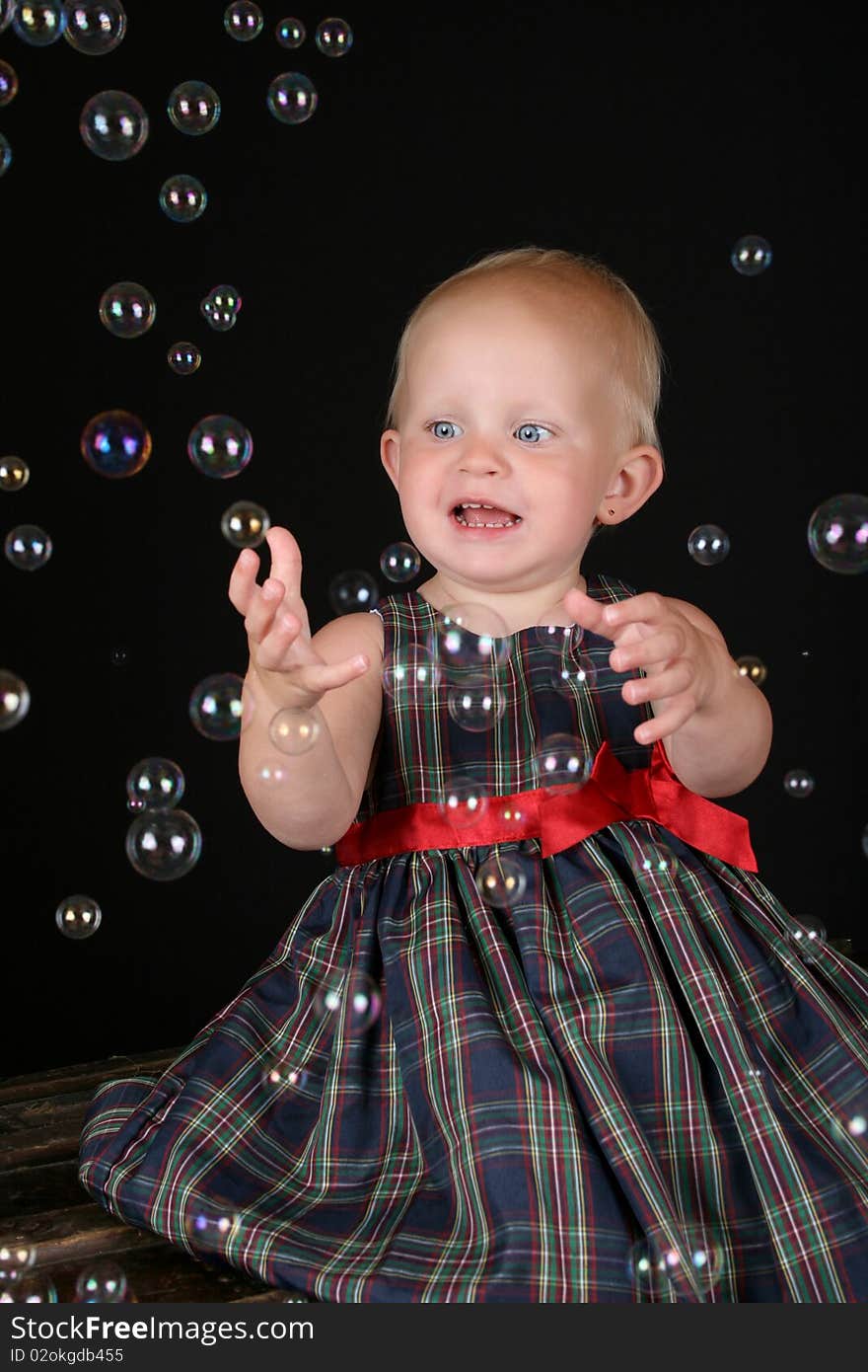 Cute blond toddler girl surrounded by bubbles sitting on a wooden trunk. Cute blond toddler girl surrounded by bubbles sitting on a wooden trunk