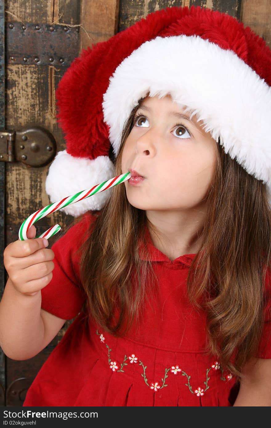 Cute brunette girl wearing a christmas hat, eating candy. Cute brunette girl wearing a christmas hat, eating candy