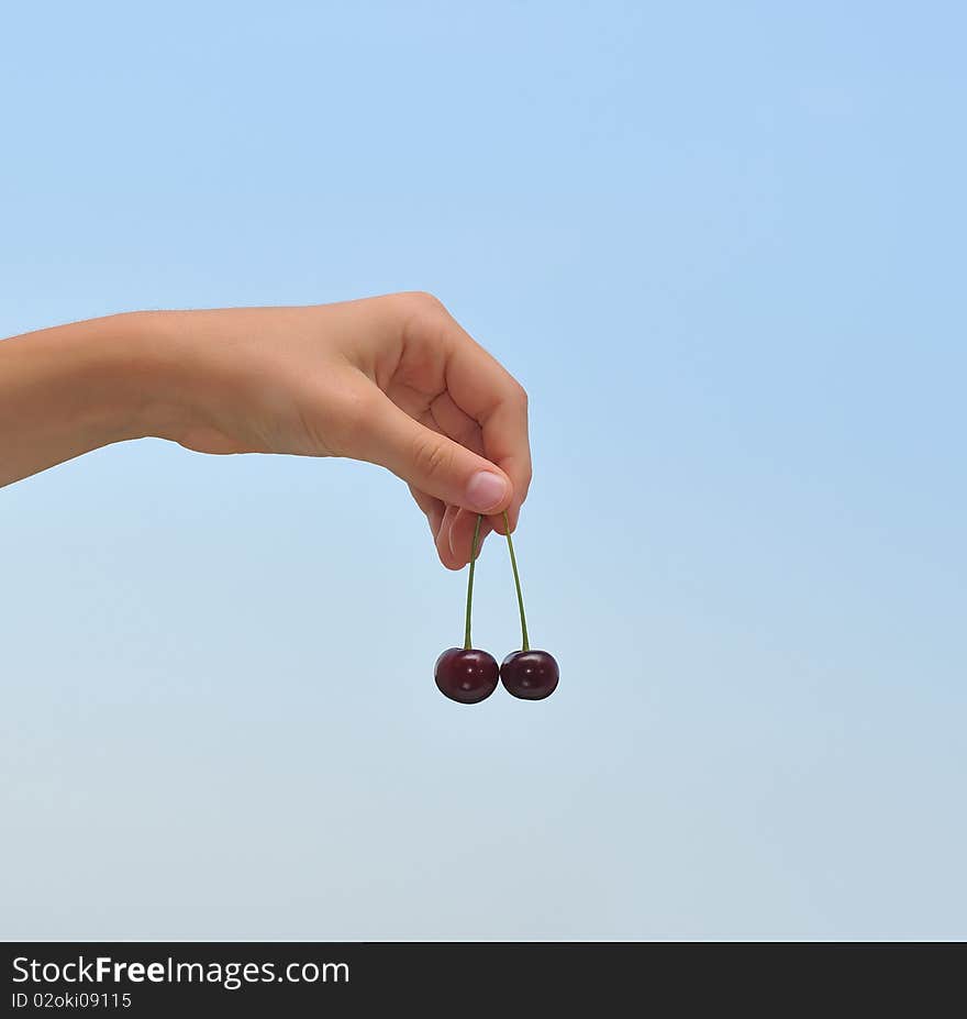 A female hand holding cherries against the sky. A female hand holding cherries against the sky.