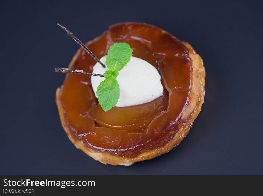 Individual apple tart Tatin with a scoop of a Chantilly cream, mint and caramelised (edible)vanilla pod. Shot from above, isolated on black.Classic french dessert