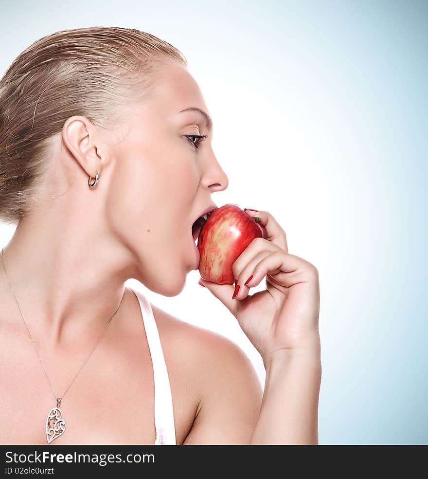 Portrait of young beautiful woman biting apple on blue back