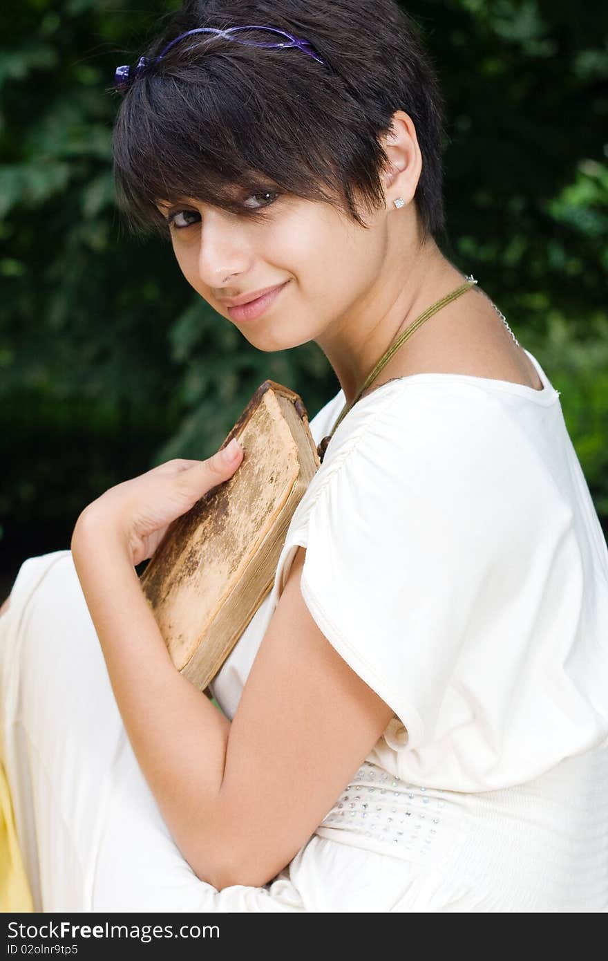 Brunette chick sitting in the park with an old book. Brunette chick sitting in the park with an old book