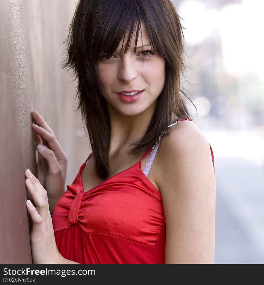 Very good looking girl leaning against a wall smiling and looking towards the camera. Very good looking girl leaning against a wall smiling and looking towards the camera