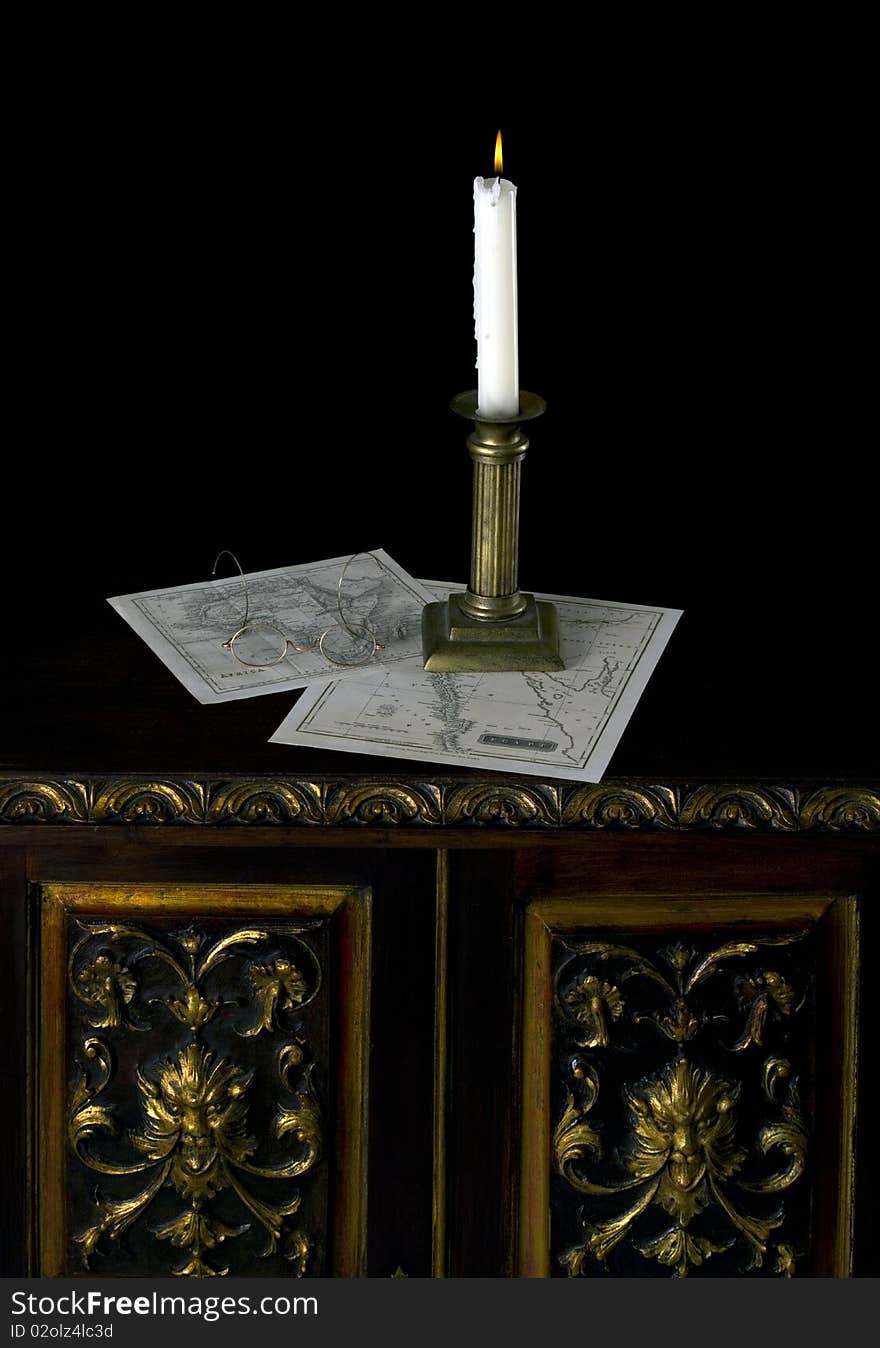 A candle with old maps in old candlestick on old table over dark background. A candle with old maps in old candlestick on old table over dark background