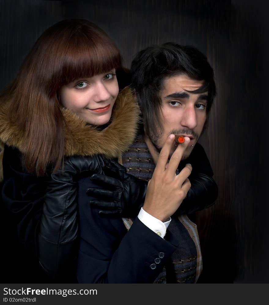 Portrait of young man and young women with cigar on dark background