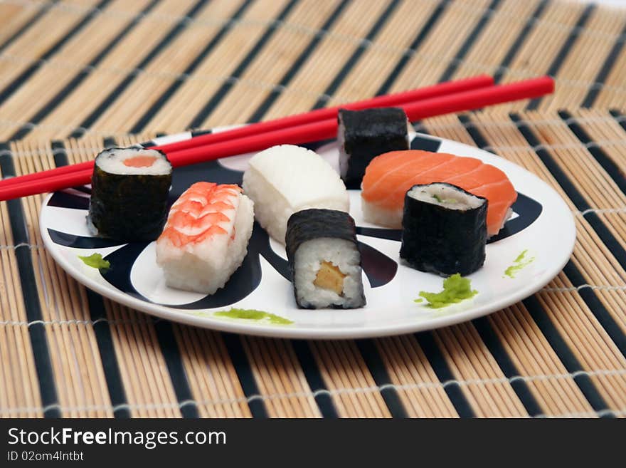 Assortment of sushi on a plate with red chopsticks on a circular decorated plate, on a wood table-cloth. Assortment of sushi on a plate with red chopsticks on a circular decorated plate, on a wood table-cloth