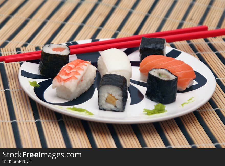 Assortment of sushi on a plate with red chopsticks and wasabi in a circular decorated plate, on a wood table-cloth. Assortment of sushi on a plate with red chopsticks and wasabi in a circular decorated plate, on a wood table-cloth